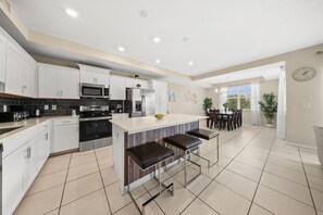 Une cuisine moderne dotée d’appareils électroménagers en acier inoxydable, d’un îlot central avec des tabourets, et d’un coin repas offrant une vue agréable.