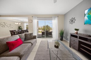 A living room with a sofa, a coffee table, a TV, and a dining area with chairs and a table. - Storey Lake: Cozy 2BR Near Disney (Kissimmee)