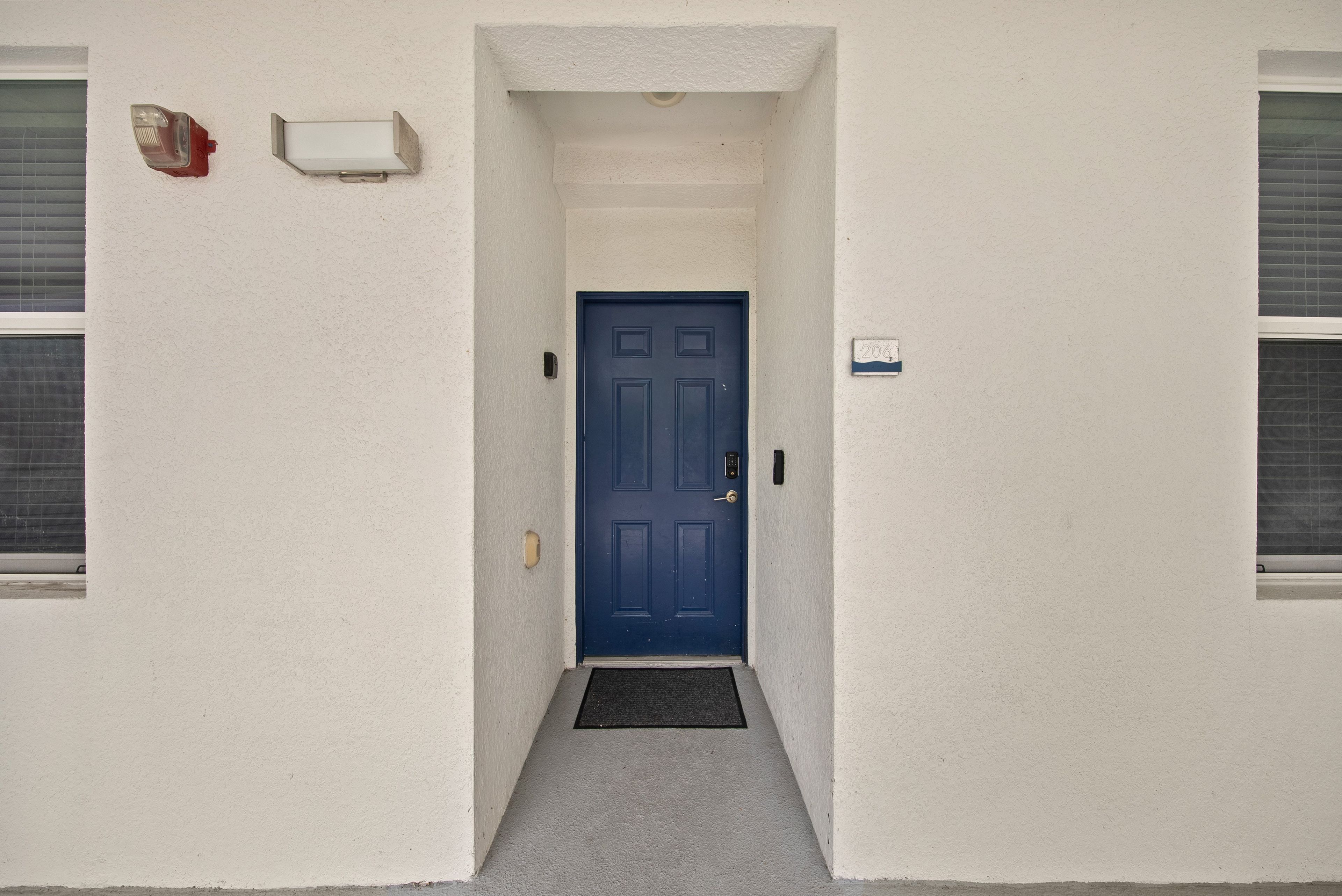 Un couloir étroit mène à une porte bleue devant laquelle se trouve un paillasson.