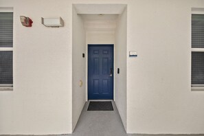 Un couloir étroit mène à une porte bleue devant laquelle se trouve un paillasson.