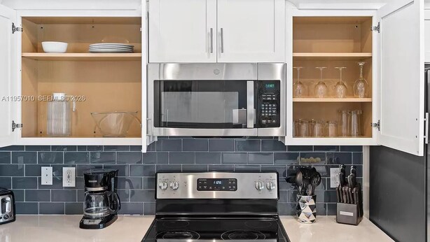 A kitchen with white cabinets, a stainless steel microwave, a black stove, and a coffee maker. - Storey Lake: Cozy 2BR Near Disney (Kissimmee)