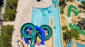 An aerial view of a swimming pool area with a water slide and surrounding landscaping. - Storey Lake: Cozy 2BR Near Disney (Kissimmee)