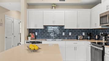 A modern kitchen with white cabinets, a black tiled backsplash, and a central island with a bowl of fruit.
