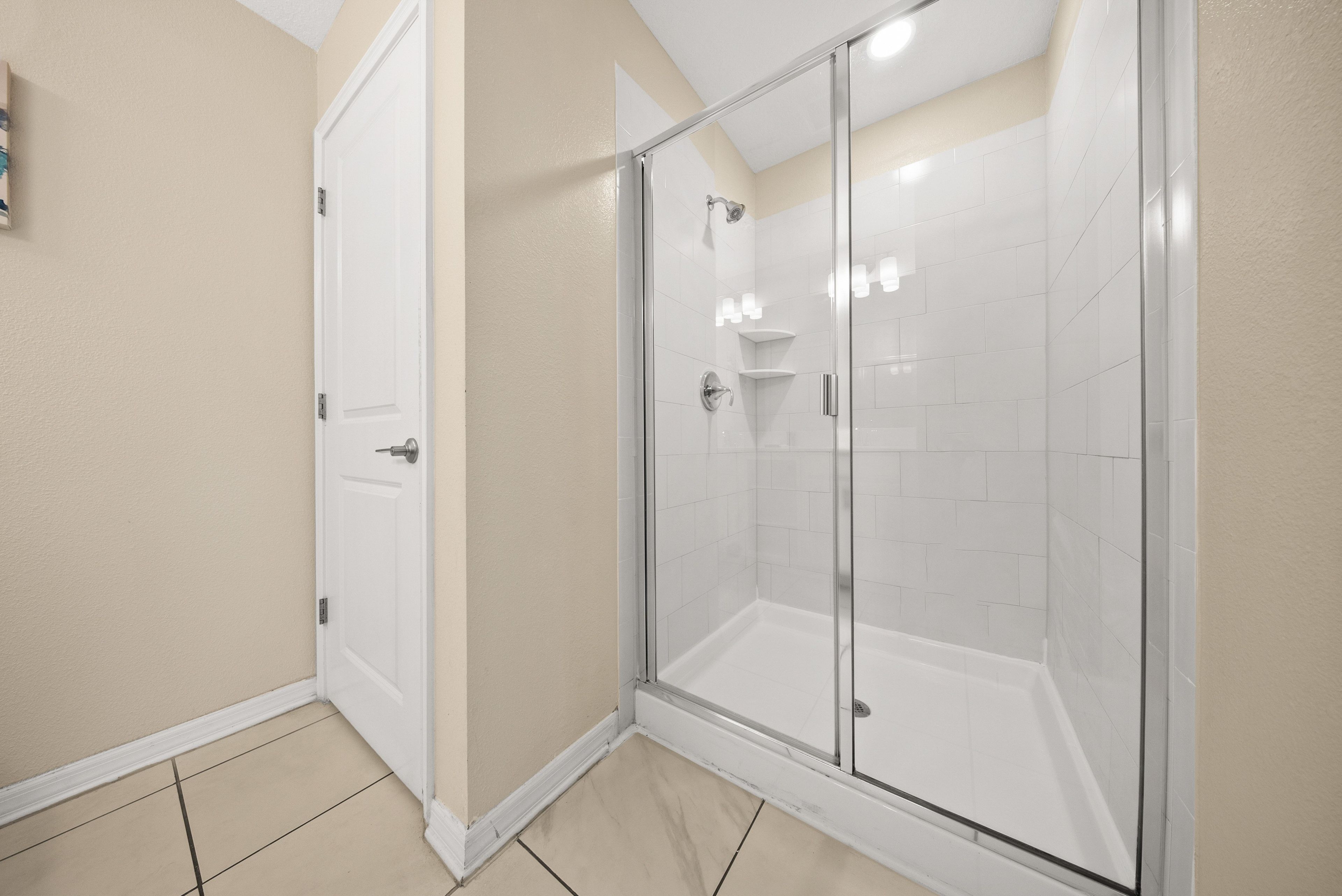 A modern bathroom with a glass-enclosed shower, white tiled walls, and a door.