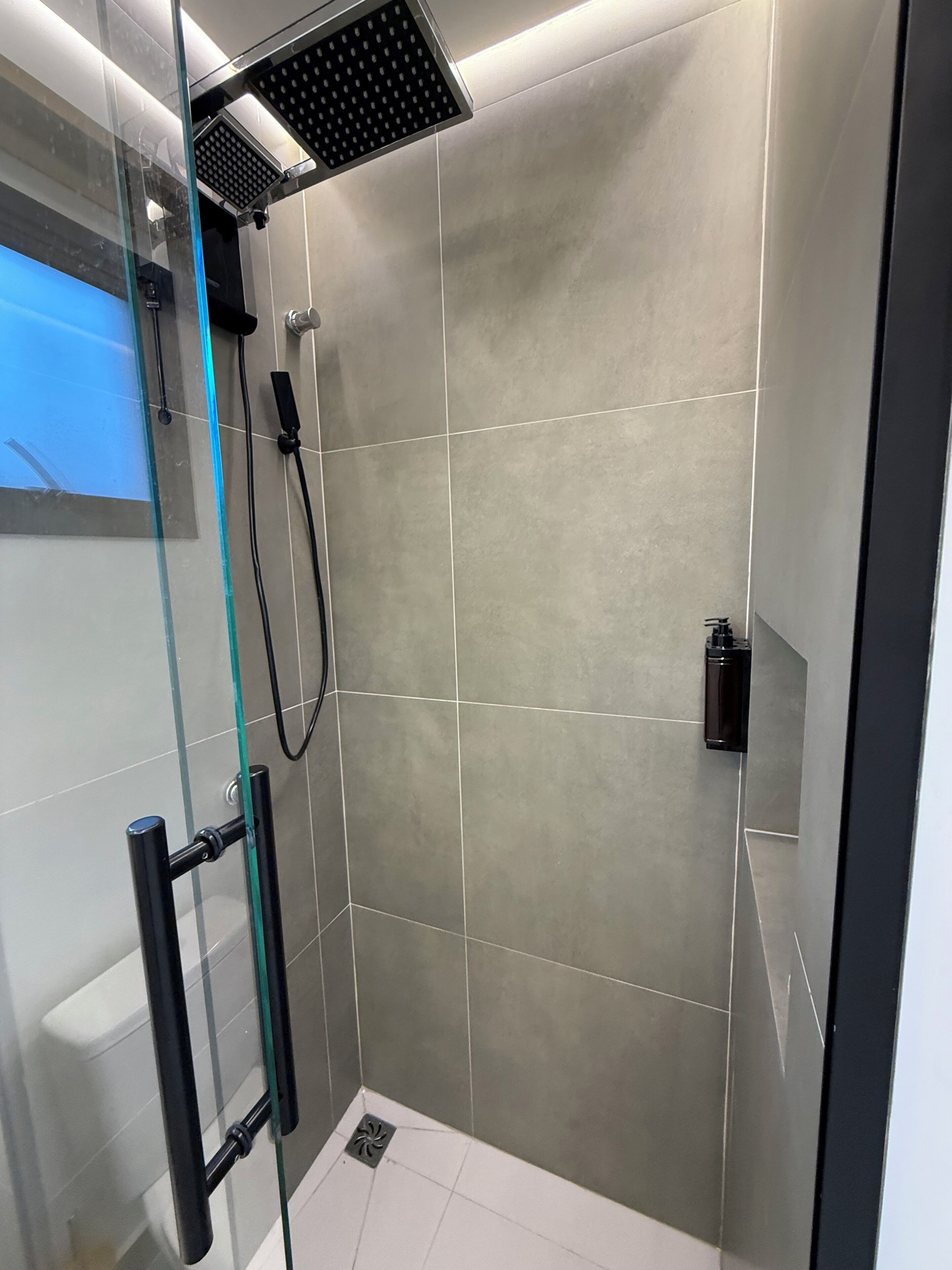 Um chuveiro moderno com porta de vidro, um chuveiro manual e painel de controle fixado na parede.