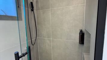 Um chuveiro moderno com porta de vidro, um chuveiro manual e painel de controle fixado na parede.