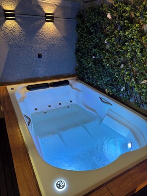 Un jacuzzi con borde de madera, rodeado por una pared cubierta de follaje verde.