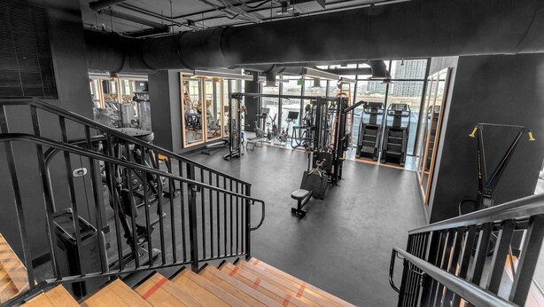 Une salle de sport équipée de matériel d’exercice, avec un escalier et de grandes fenêtres.