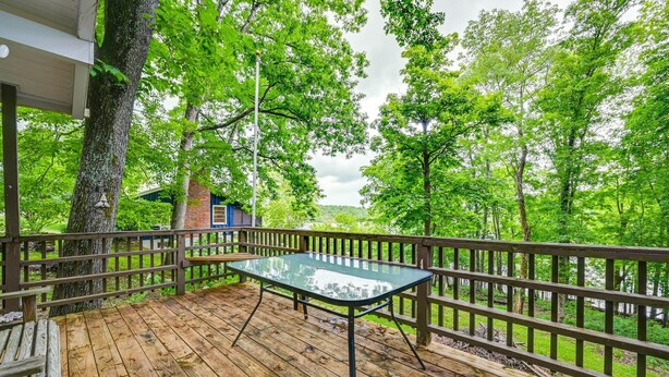 A wooden deck with a glass table, surrounded by a wooden railing, overlooking a forested area. - Waterfront Nolin Lake Retreat: Lake Views (Ollie)