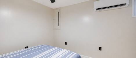 Een slaapkamer met een bed, een plafondventilator, een airconditioning en een raam.