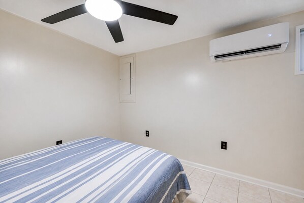 A bedroom with a bed, a ceiling fan, an air conditioning unit, and a window.