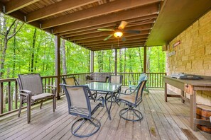 A covered outdoor deck with a table and chairs, surrounded by trees.