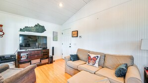 A living room with a sofa, a television, a wooden cabinet, and a wall-mounted decorative piece. - Waterfront Nolin Lake Retreat: Lake Views (Ollie)