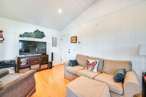 A living room with a sofa, a television, a wooden cabinet, and a wall-mounted decorative piece. - Waterfront Nolin Lake Retreat: Lake Views (Ollie)