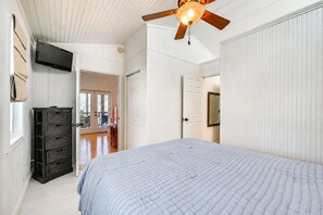 Un dormitorio con cama, ventilador de techo, televisor y cómoda.