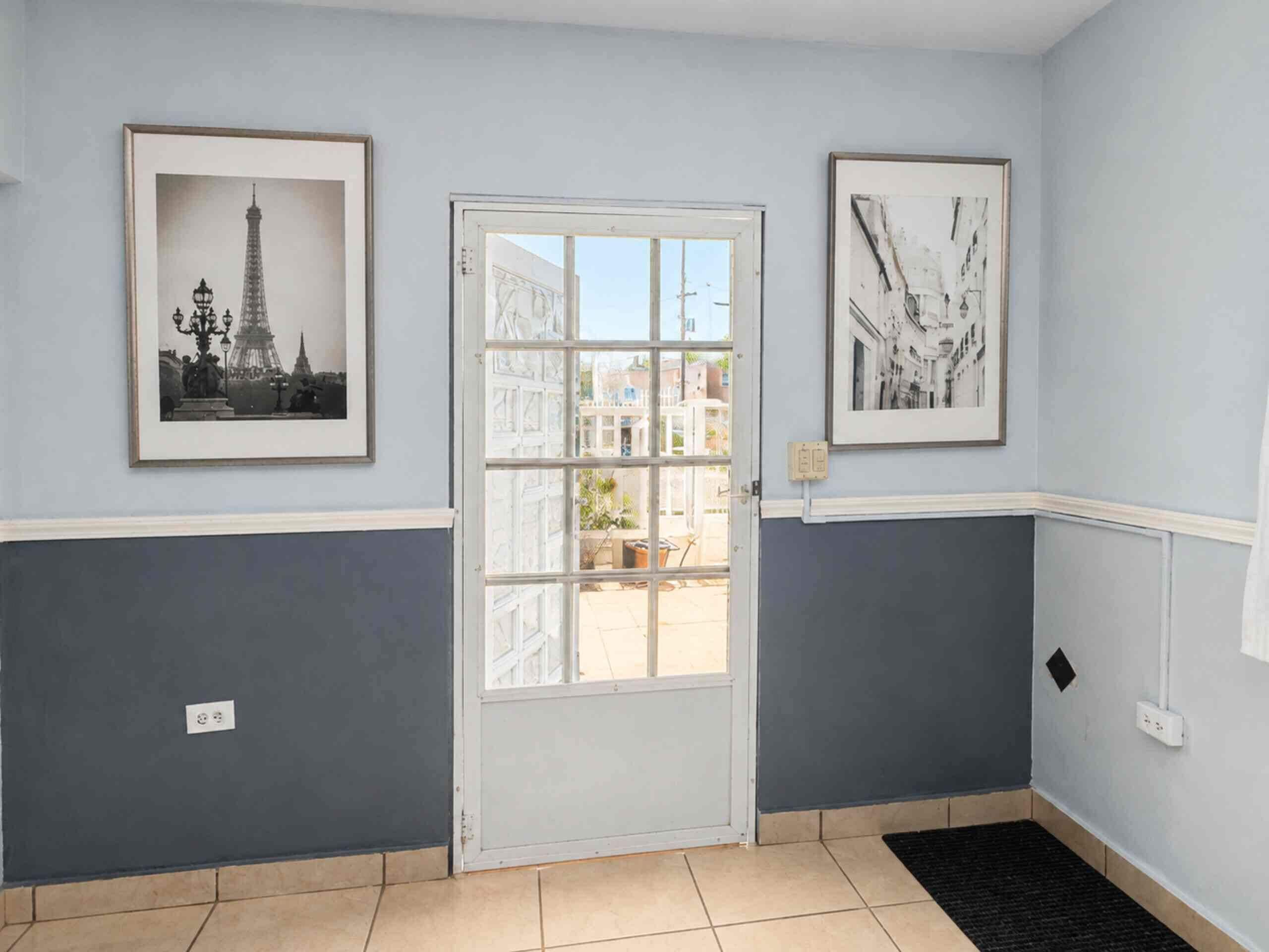 A hallway with a white door, two framed pictures, and a tiled floor.