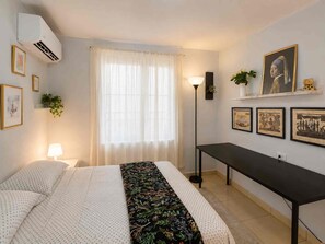 A hotel room with a bed, a desk, a lamp, and artwork on the walls.