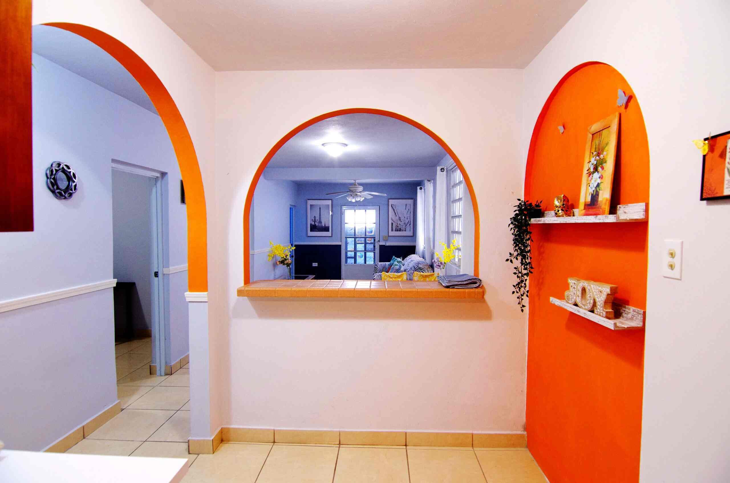 Un couloir avec une arche centrale menant à une pièce dotée d’un ventilateur de plafond, d’une fenêtre et d’une porte.