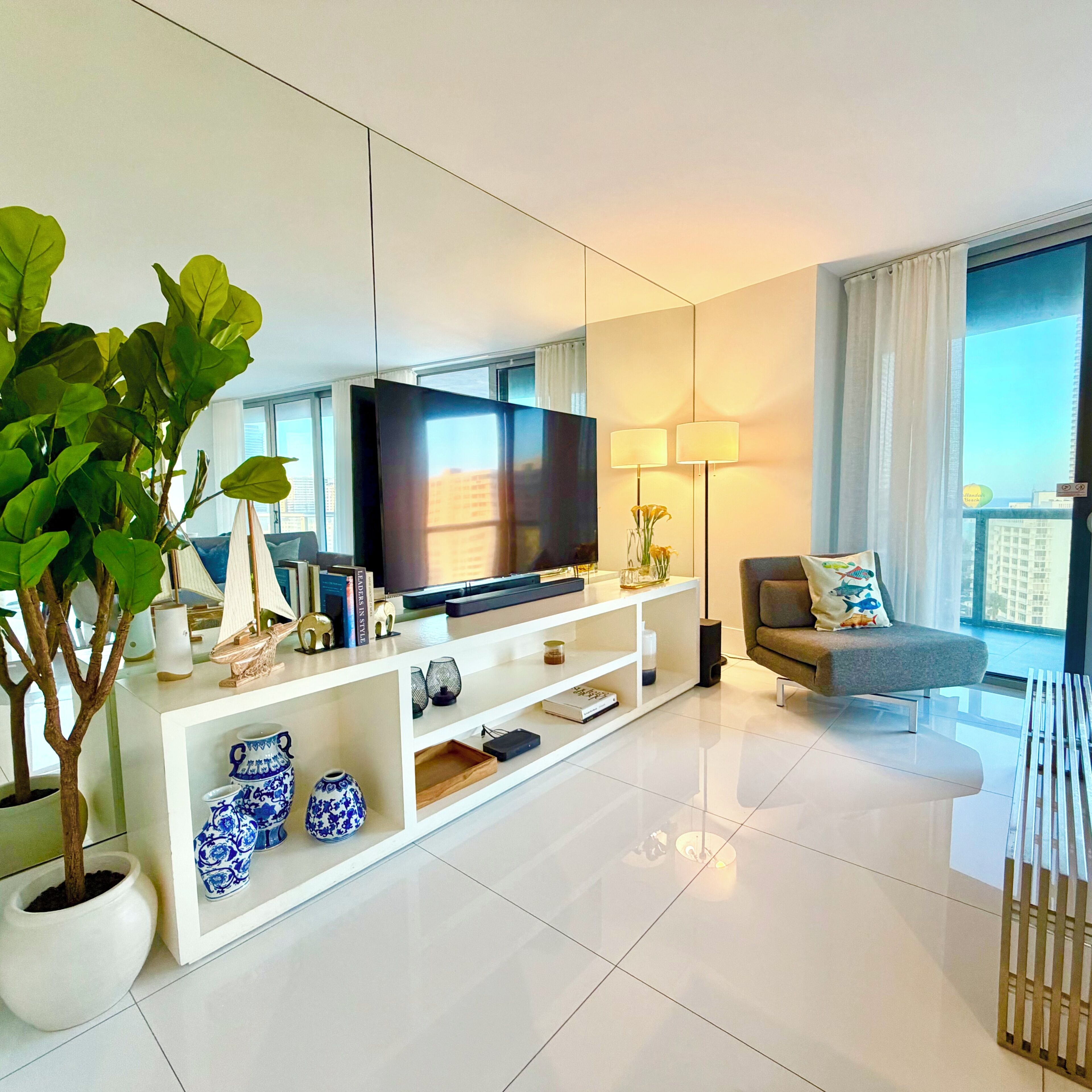 A modern living room with a flat-screen TV, a sofa, a potted plant, and decorative items on a white console.