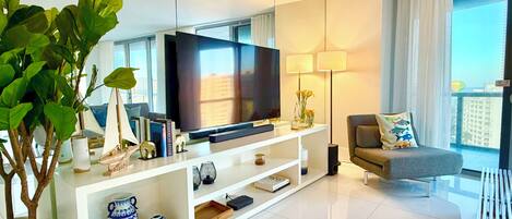 Una sala de estar moderna con un televisor de pantalla plana, un sofá, una planta en maceta y objetos decorativos sobre un mueble blanco.