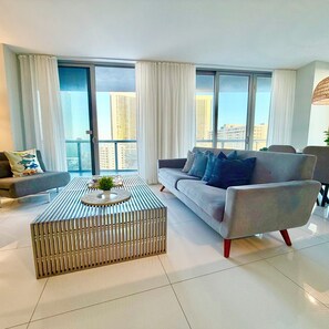 Ein modernes Wohnzimmer mit einer Couch, einem Couchtisch und Blick auf die Stadt durch große Fenster.
