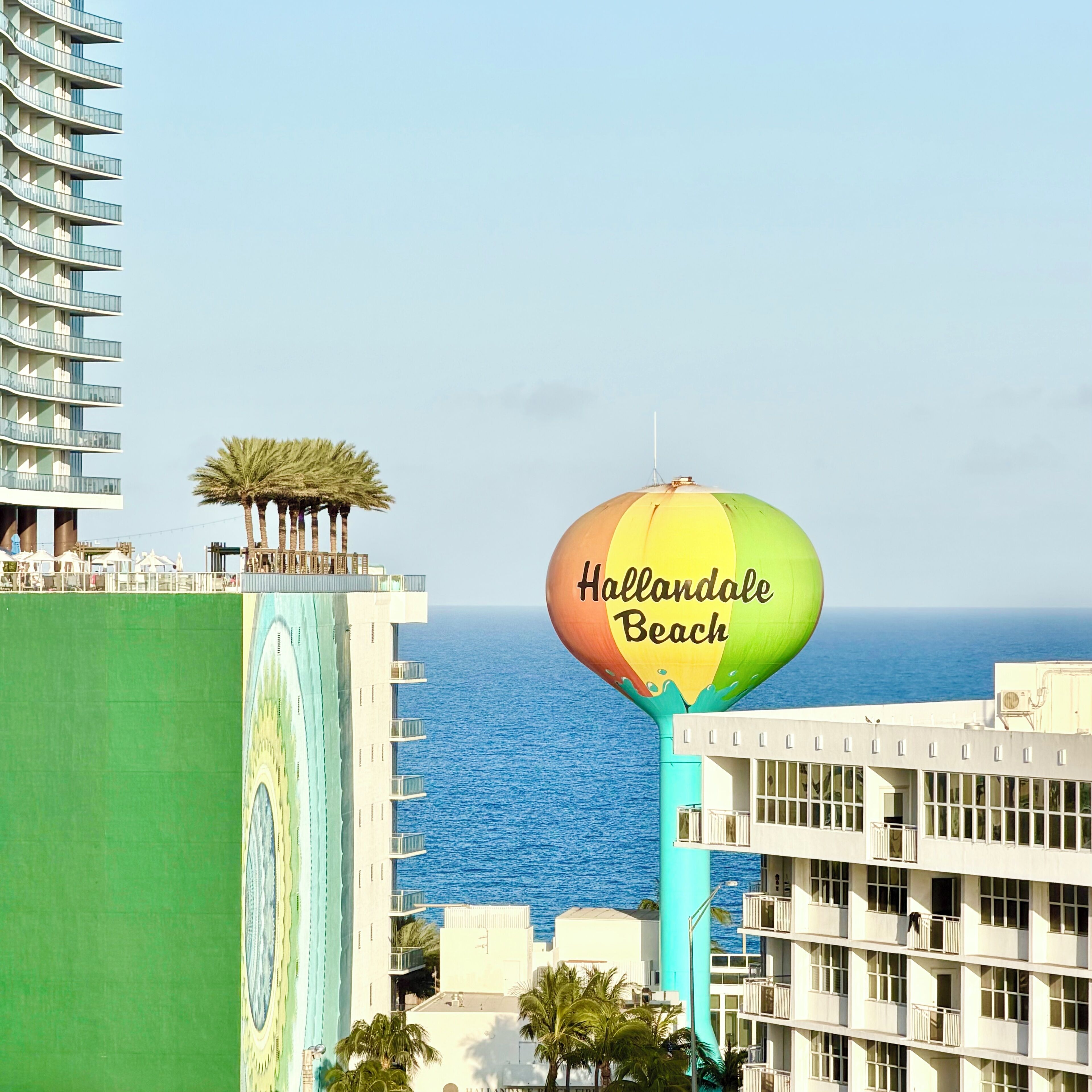 A view of a coastal area with a prominent building featuring a balcony and a colorful hot air balloon with 'Hollandale Beach' written on it.