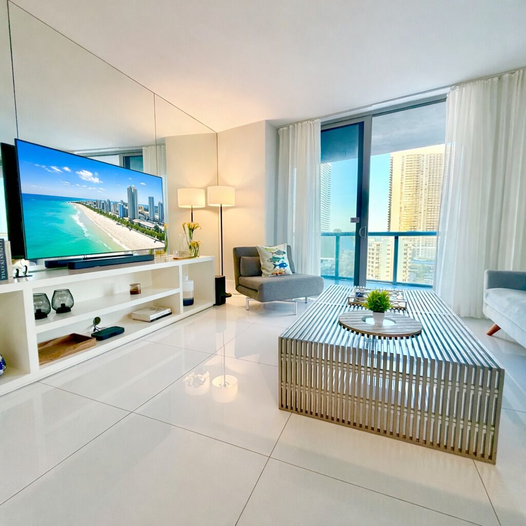 Een moderne woonkamer met een flatscreen televisie, een bank, een salontafel en een balkon met uitzicht op de stad.