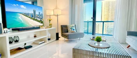 Un salón moderno con televisor de pantalla plana, sofá, mesa de centro y balcón con vistas a la ciudad.