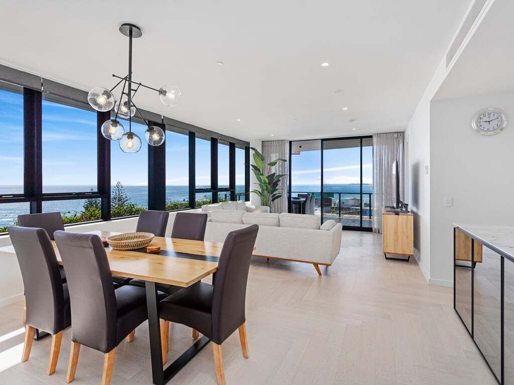 Una sala de estar moderna con comedor, ventanas amplias y vista al mar.