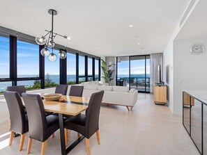A modern living room with a dining area, large windows, and a view of the sea. - Magnoli Palm Beach Penthouse | Oceanfront Luxury Escape (Gold Coast)