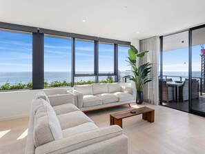 En moderne stue med sofa, sofabord og store vinduer med udsigt over havet.