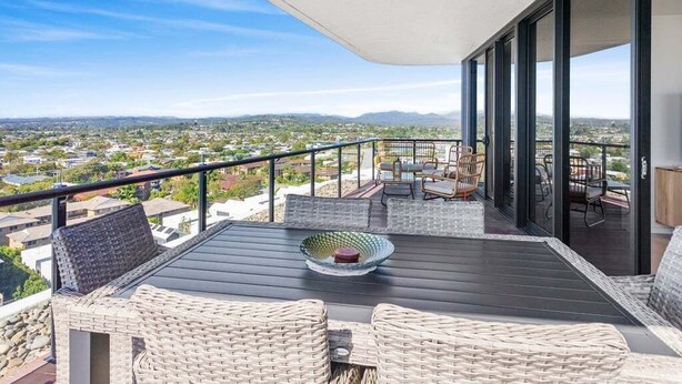 A balcony with wicker furniture, a table, and a view of a cityscape.