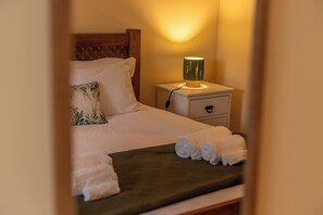 A neatly made bed with white linens, a green throw blanket, and rolled towels on a wooden headboard. - Phenomenal 3-bedroom house in Santo António With fantastic view and hiking trail (Santo António)
