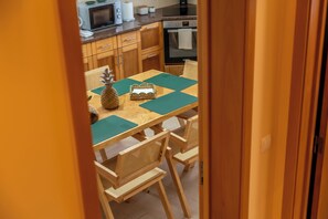 A wooden dining table with a woven placemat, surrounded by woven chairs, in a kitchen with wooden cabinets and appliances. - Phenomenal 3-bedroom house in Santo António With fantastic view and hiking trail (Santo António)
