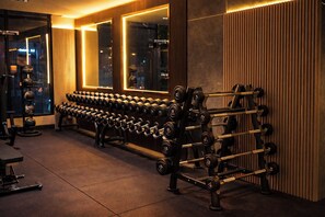 Ein Fitnessstudio mit Reihen von Kurzhanteln und Langhanteln, großen Spiegeln und einem Fenster mit Blick auf die Stadt.