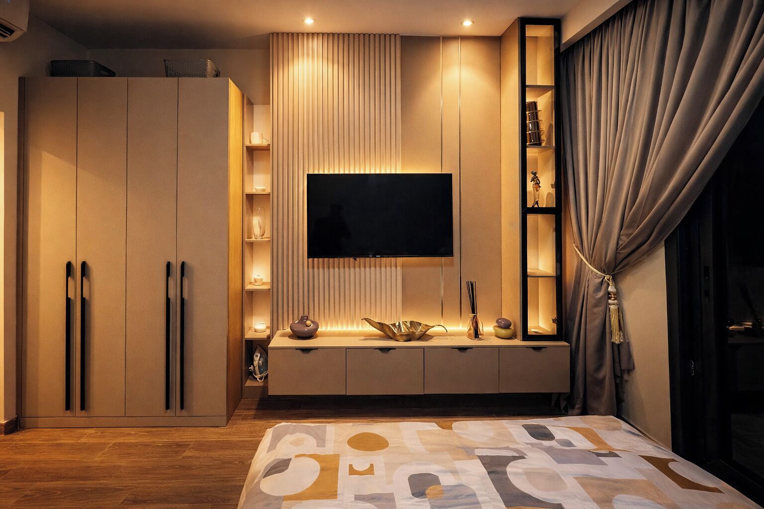 A modern bedroom with a large bed, a TV mounted on the wall, built-in cabinets, and a bedside table with decorative items.