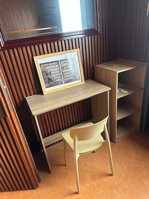 A small wooden desk with a framed motivational quote, a white chair, and a slanted shelf.