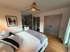 Een slaapkamer met een bed, een plafondventilator, een ingelijst schilderij aan de muur en een zichtbare badkamer door een open deur.