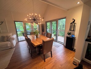 Een ruime eetruimte met een houten tafel en stoelen, een kroonluchter en grote schuifdeuren die leiden naar een terras.