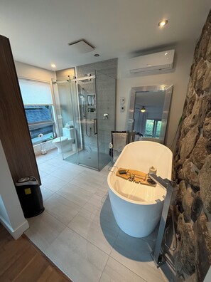 A modern bathroom with a large bathtub, a glass shower enclosure, and a stone accent wall. - Country House for Winter Sports (Magog)