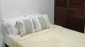 A bed with white bedding and two pillows, a wooden wardrobe, and a white wall. - Family-Friendly 3-Bedroom Apartment Near San Felipe Castle (cartagena)
