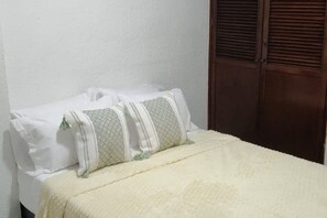 A bed with white bedding and two pillows, a wooden wardrobe, and a white wall. - Family-Friendly 3-Bedroom Apartment Near San Felipe Castle (cartagena)