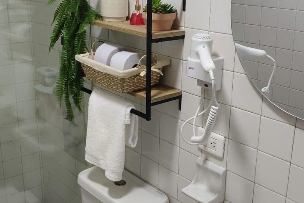 Een badkamer met een wit toilet, een handdoekhouder, een plank met een mand, een haardroger en een plant.