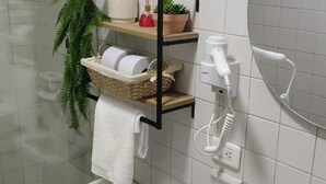 A bathroom with a white toilet, a towel rack, a shelf with a basket, a hairdryer, and a plant. - Family-Friendly 3-Bedroom Apartment Near San Felipe Castle (cartagena)