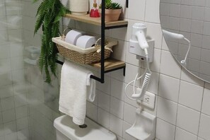A bathroom with a white toilet, a towel rack, a shelf with a basket, a hairdryer, and a plant. - Family-Friendly 3-Bedroom Apartment Near San Felipe Castle (cartagena)
