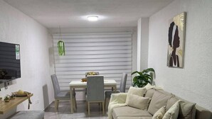 A modern living room with a sofa, a dining table, chairs, a TV, and a plant. - Family-Friendly 3-Bedroom Apartment Near San Felipe Castle (cartagena)