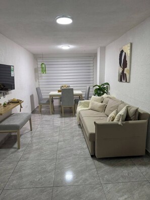 A modern living room with a sofa, a dining table, chairs, a TV, and a plant. - Family-Friendly 3-Bedroom Apartment Near San Felipe Castle (cartagena)
