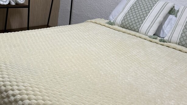 A bed with a textured white blanket, a pillow with a geometric pattern, and a shelf with rolled towels. - Family-Friendly 3-Bedroom Apartment Near San Felipe Castle (cartagena)