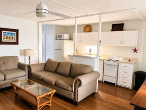 A compact living space with a sofa, a glass-top coffee table, a kitchenette with a stove, microwave, and cabinets. - Make Memories in Paradise at Long Reef (Christiansted)