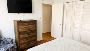 Un dormitorio con una cama, un aparador de madera, un televisor montado en la pared y un armario con puertas batientes.